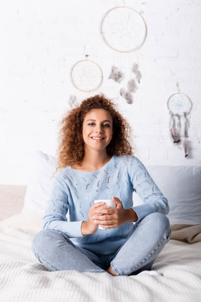 istock Selective focus of young woman looking at camera while holding cup on bed 1276432289