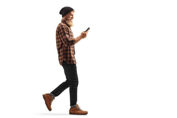 istock Hipster guy with beard and mustache walking and using a mobile phone 1276432412
