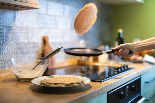 Close-up of man's hand tossing pancakes on pan in the kitchen.