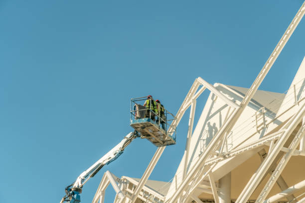 istock Painter, plasterer in special clothes, paint the facade of the building with white paint roller at the height of the cradle on a sunny day against the blue sky. 1276435876