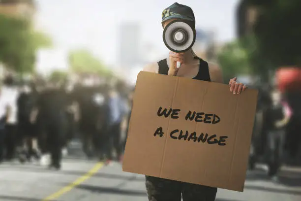 Photo of public protest and riots in the city streets. woman with megaphoen and cardboard poster in hands on protesters crowd background. democracy concept