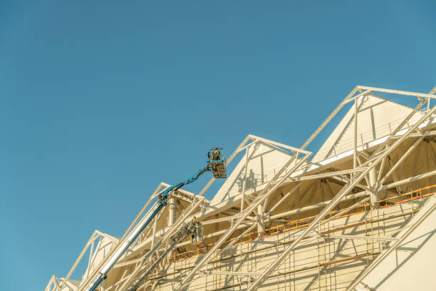 istock Painter, plasterer in special clothes, paint the facade of the building with white paint roller at the height of the cradle on a sunny day against the blue sky. 1276438405