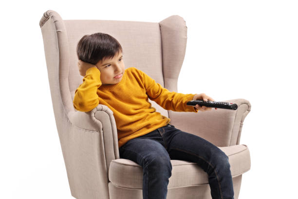 istock Boy sitting in an armchair and holding a remote control 1276438638