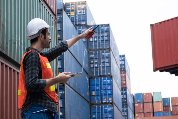 istock Engineer worker or technical standing and point out in the container yard shipping area and used radio communication to control loading containers into the stack. Industrial and import-export concept 1276438939