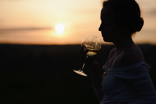 Young woman silhouette drinking wine on the hill at sunset. High quality photo