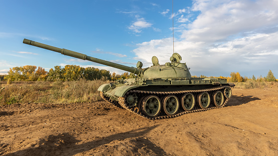 A side shot of old russian tank T-62 in the field. Blue cloudy sky as a background.