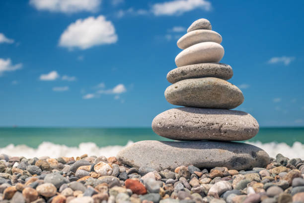 pyramid of sea pebbles on the beach against the backdrop of the sea wave in sunny day. concept of balance harmony and meditation. copy space pyramid of sea pebbles on the beach against the backdrop of the sea wave in sunny day. concept of balance harmony and meditation. copy space simple living stock pictures, royalty-free photos & images