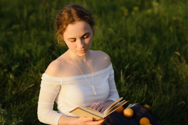 istock Young girl is reading a book and sitting on the grass while sun is setting down. Summer feeling 1276443901