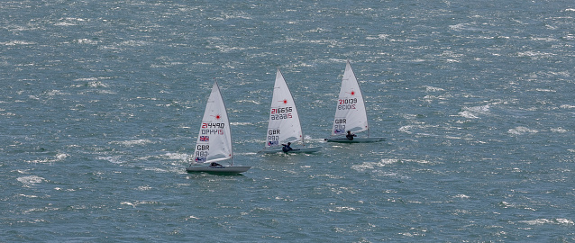 Portland harbour, United Kingdom - July 3, 2020: High Angle aerial panoramic shot of three laser class racing dinghies sailing close to each other in Portland harbour.