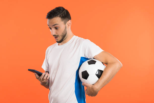 fan de football ou joueur regardant le smartphone étonné et retenant un football sous le bras - fan hooligan screaming shouting photos et images de collection