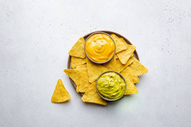 Nachos chips with sauces Nachos chips in a bowl with sauces guacamole and cheese, dip variety, over white stone background, top view. nacho chip stock pictures, royalty-free photos & images