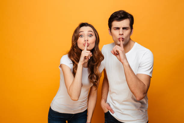 istock Mystery young couple posing together and showing silence gestures 1276446400