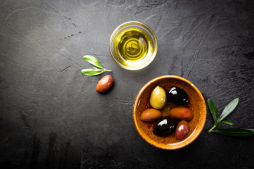 Black and green olives and olive oil in wooden bowls on black background. Top view with copy space for text.