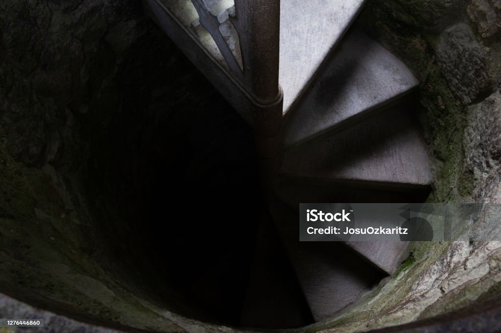 Stone spiral staircase Top view of spiral staircase leading from light into darkness. Going towards the unknown, fear, afraid concepts Moving Down Stock Photo