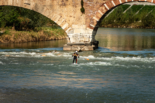 Verona, Italy - Sept 19th, 2020: Verona, a man on his Stand up Paddleboarding (SUP) paddling in the rapids of the River Adige, Ponte Pietra (Stone Bridge), Veneto, Italy, Europe.