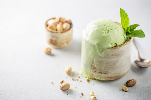Homemade pistachio ice cream scoop with chopped pistachios on white background