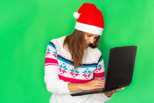 크리스마스 온라인 쇼핑. 녹색 유니폼 배경에 노트북과 새해 모자를 쓴 소녀. - 4772 뉴스 사진 이미지
