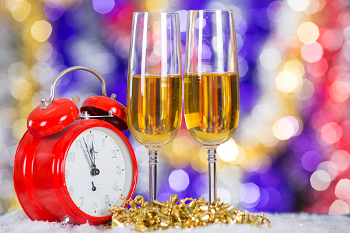 Christmas and New Year decoration - champagne glasses, Christmas tree ornaments and a clock with colorful glitter background.