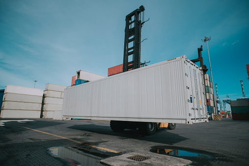 Forklift truck lifting cargo container in shipping yard or dock yard with cargo container stack