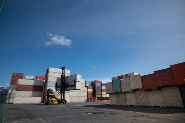 istock Forklift truck lifting cargo container in shipping yard or dock yard with cargo container stack 1276461039