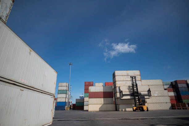 istock Forklift truck lifting cargo container in shipping yard or dock yard with cargo container stack 1276461042