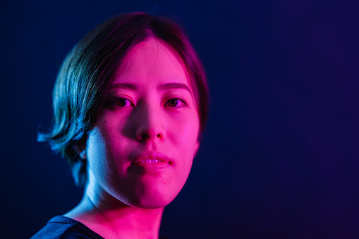 A portrait of a young woman lit by neon colored lights.