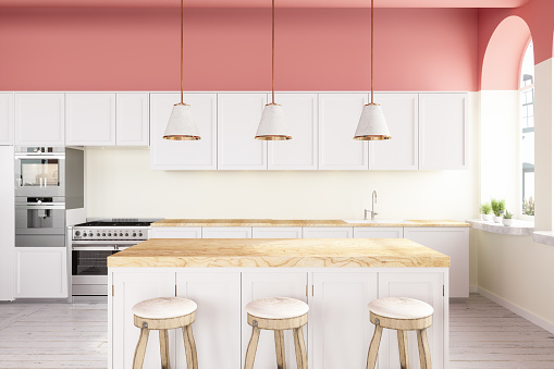 Cocina amurallada rosa con armarios blancos, luces colgantes, isla de cocina y suelo de madera photo