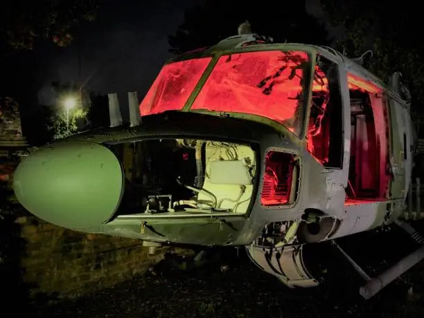 Photo of disused abandoned Helicopter grounded at night with red lighting to show nose body component parts and lit windows