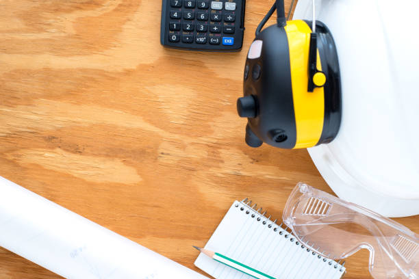 istock Flat lay of engineering stuff / PPE (Personal Protection Equipment) contain engineering drawing, pencil, safety glasses, hardhat calculator for planning or calculate engineering work on wooden desk. 1276465982