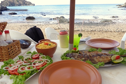 A table with lots of dish food fish salad and drinks. At the beach, looking to the ocean at Fernando de noronha, Brazil