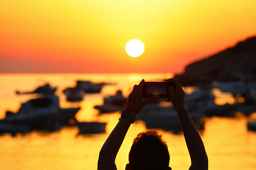 Hands holding a mobile phone and making photography of the sunset  or sunrise on the beach