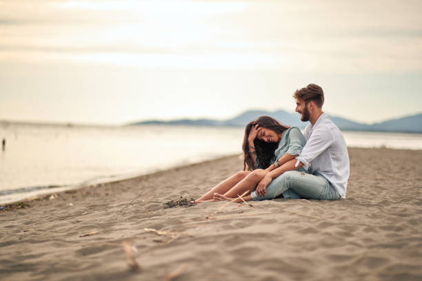 istock Young lovers sitting in a hug on the beach 1276471084