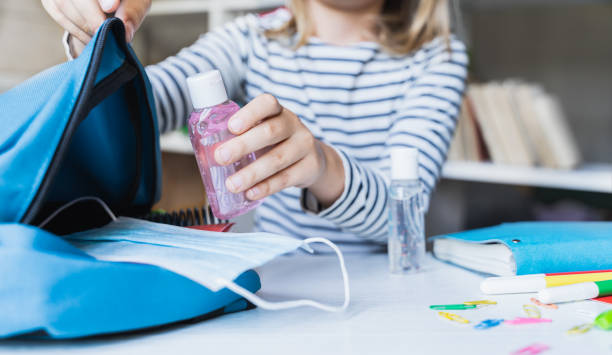 Little girl packing blue backpack in kids's room. Face mask, bottle of sanitizer, stationery, pens, multicolored markers, notebooks. Back to school. Mom's hygiene,safety precautions after coronavirus. niña empacando mochila azul en la habitación de los niños. máscara facial, botella de desinfectante, papelería, bolígrafos, marcadores multicolores, cuadernos. regreso a la escuela. higiene de la madre, precauciones de seguridad después del coronavi