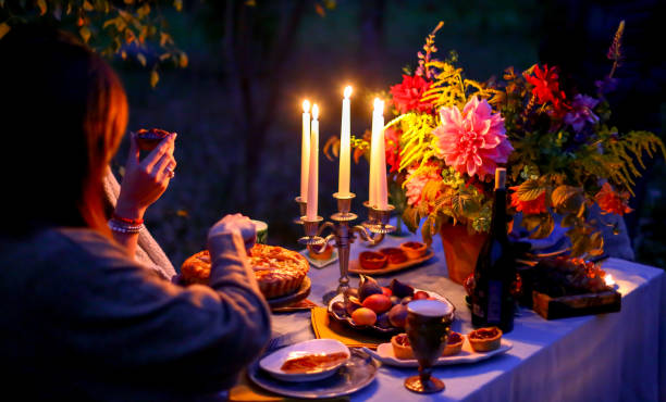 Autumn evening photo shoot. Young woman cut cake with knife. Romantic dinner at twilight nature outdoors. Table decoration closeup - figs, plates, candelabra with candles, flowers. Red dahlia bouquet. sesión de fotos de otoño por la noche. una joven cortó el pastel con un cuchillo. cena romántica en la naturaleza del crepúsculo al aire libre. decoración de la mesa de primer plano - higos, platos, candelabro con velas, flores. ramo de dahlia roja
