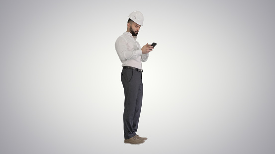Wide shot. Side view. Smart engineer in white shirt and safety engineering hat using smartphone on gradient background. Professional shot in 4K resolution. 044. You can use it e.g. in your medical, commercial video, business, presentation, broadcast