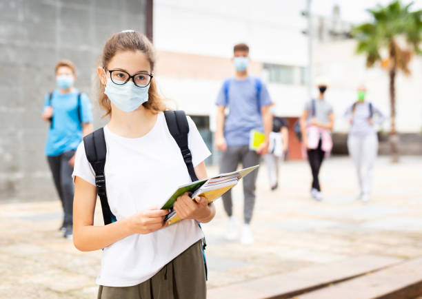 Girl in protective mask with a backpack and notebooks going to college Girl in a protective mask with a backpack and notebooks going to college 12 17 months stock pictures, royalty-free photos & images