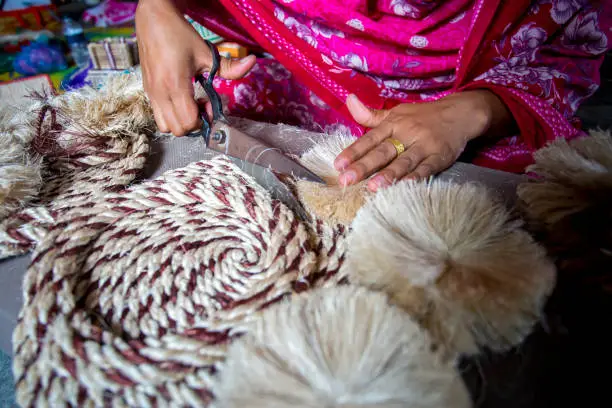 A woman making handicrafts is smoothing the fibers of a banana tree with scissors in Madhupur, Tangail, Bangladesh.