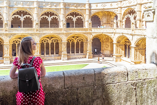 Lisbon, Portugal - May 12, 2019: Tourist with small backpack admiring architecture of cloister in Jeronimos Monastery.