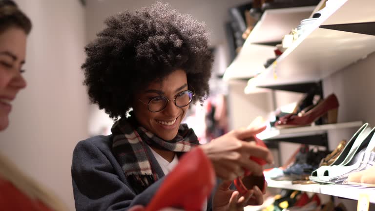 Young woman being helped by a saleswoman while shopping for shoes in a thrift store