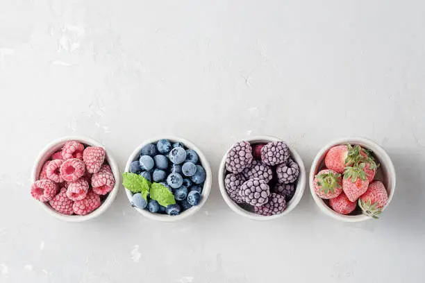 Photo of Frozen berries in small bowls on a concrete background from copies of space.