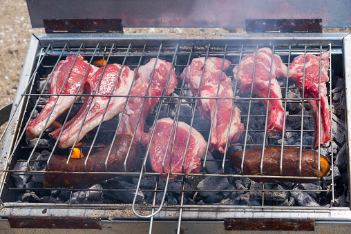 Lamb chops marinated with thyme are cooking on a barbecue outdoors.