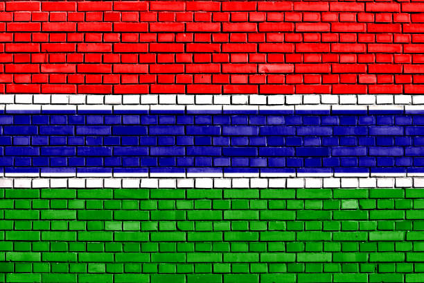 The Gambia Flag Against City Blurred Background At Sunrise Backlight