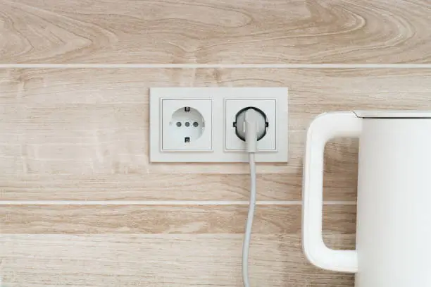Photo of White electric power sockets on wall background with plugged electric kettle into a kitchen, copy space.