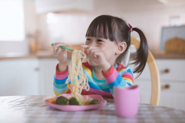 istock young girl eating spaghetti with fresh vegetable against real kitchen background 1276504549