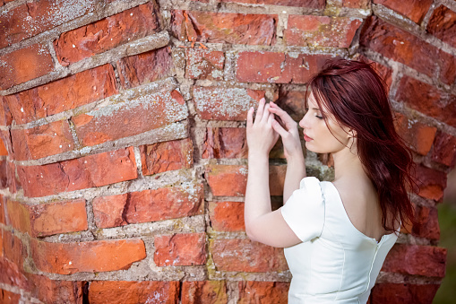 Relaxed Casucasian Red-Haired Female Against Unique Ancient Brick Wall Outdoors.Horizontal Image