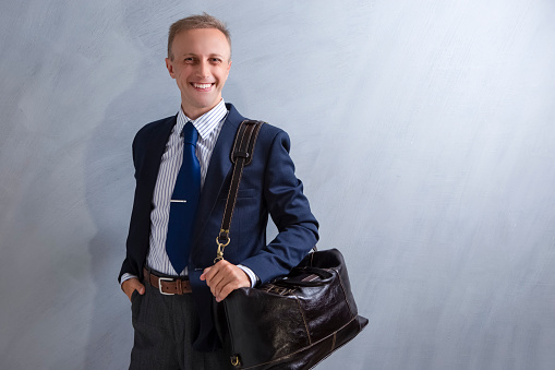 Portrait of Positive Caucasian Male Businessman with Leather Messenger bag. Posing Against Grey Wall.Horizontal image