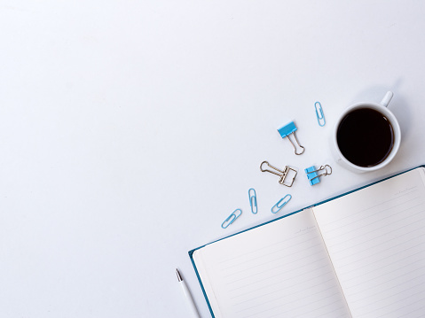 Coffee cup, notebook and paper clip materials in the corner on white background