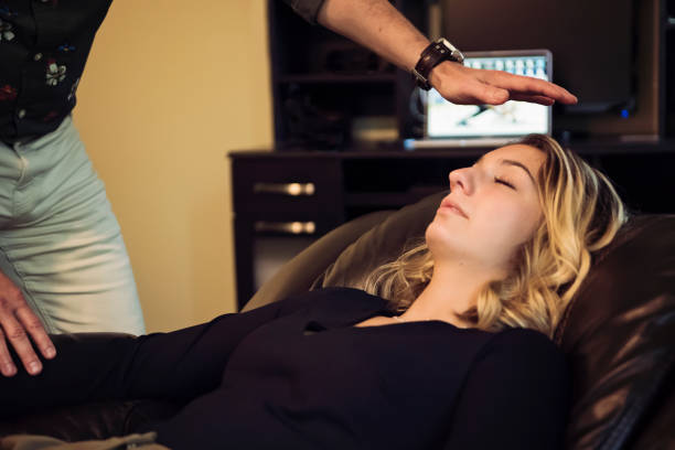 Young woman with hypnotherapist in session. Young woman in hypnosis session with mature man hypnotherapist. Both are  wearing casual clothes. She is lying down for hypnotherapy session. Horizontal waist up indoors shot with copy space. hypnosis stock pictures, royalty-free photos & images