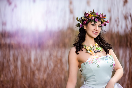 Beautiful Portrait of Caucasian Brunette Lady with Unique Flowery Chaplet and Butterflies. Posing Against Nature Background.Horizontal Image Composition