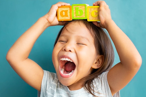 A cute little girl with a big smile holding abc blocks on top of her head in her classroom at school.